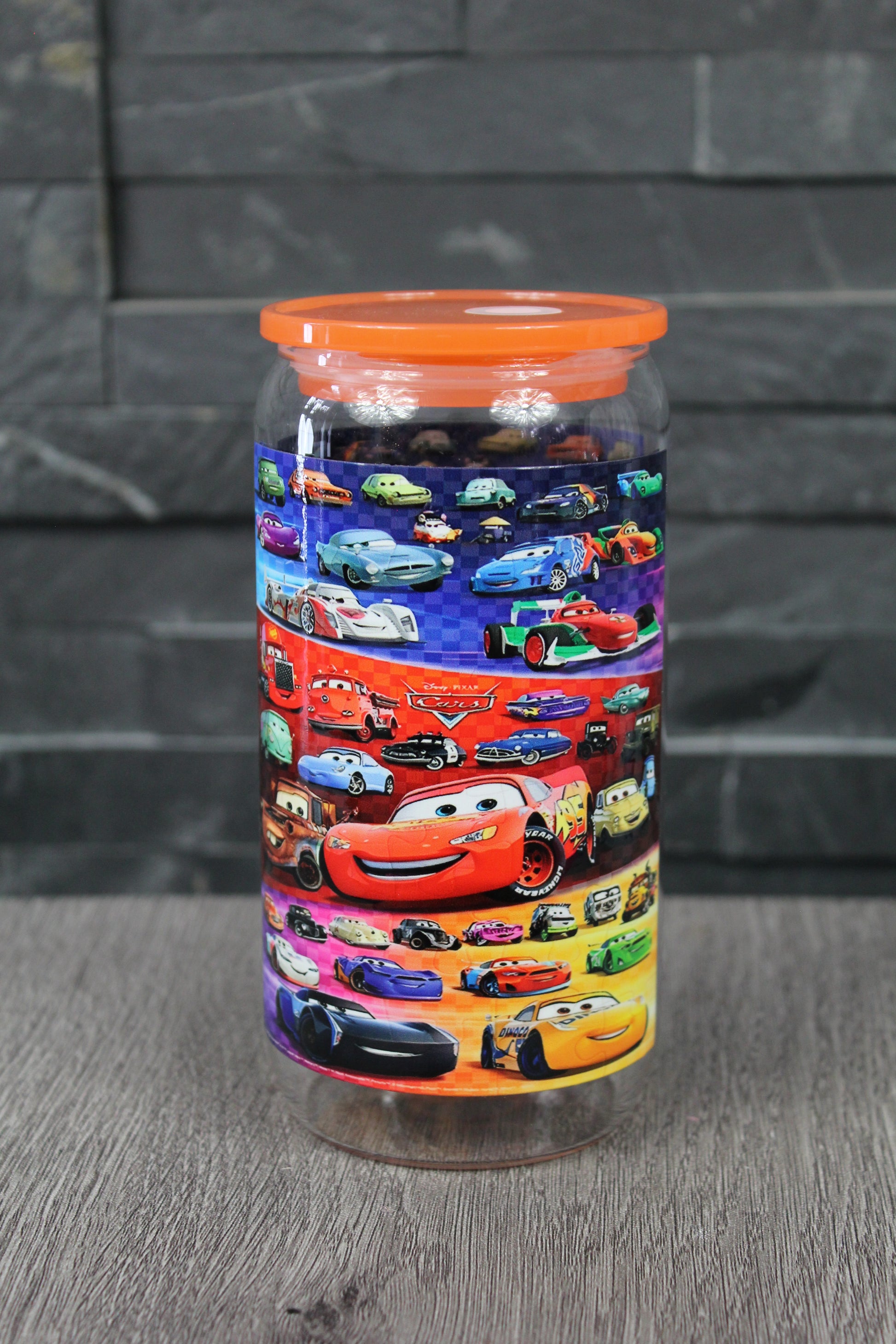 Canette 16 oz avec couvercle orange et paille, design univers voitures de course coloré, photo sur fond gris.