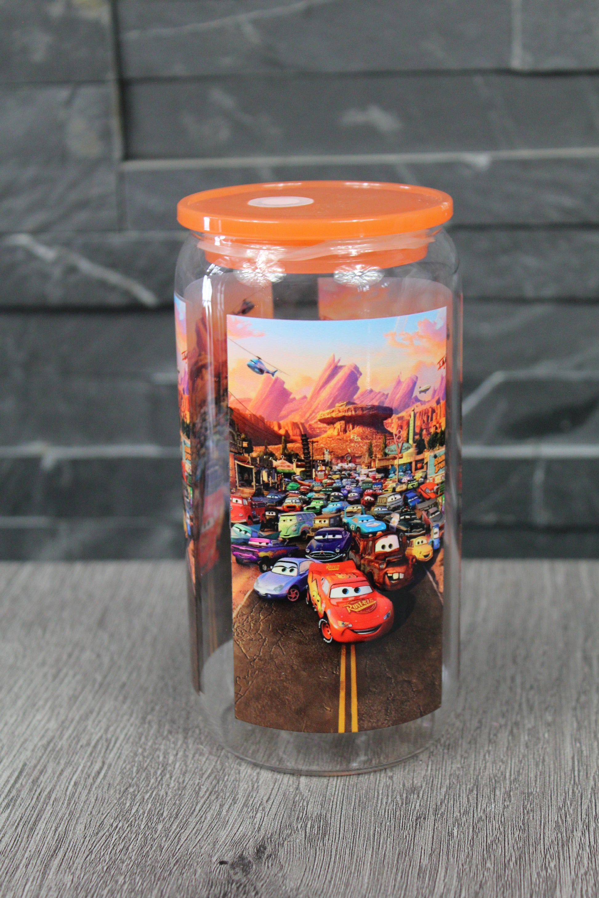 Canette 16 oz avec couvercle orange, design course automobile coloré, photo sur fond gris.